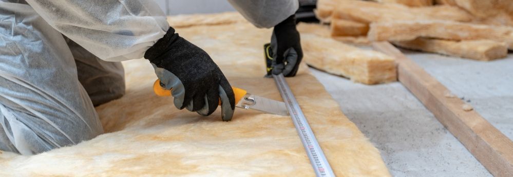 Eine Person in Schutzkleidung schneidet Dämmmaterial mit einem Messer zu.